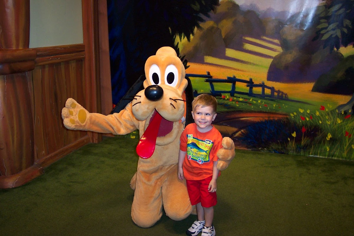 A young boy smiling next to Pluto at Walt Disney World