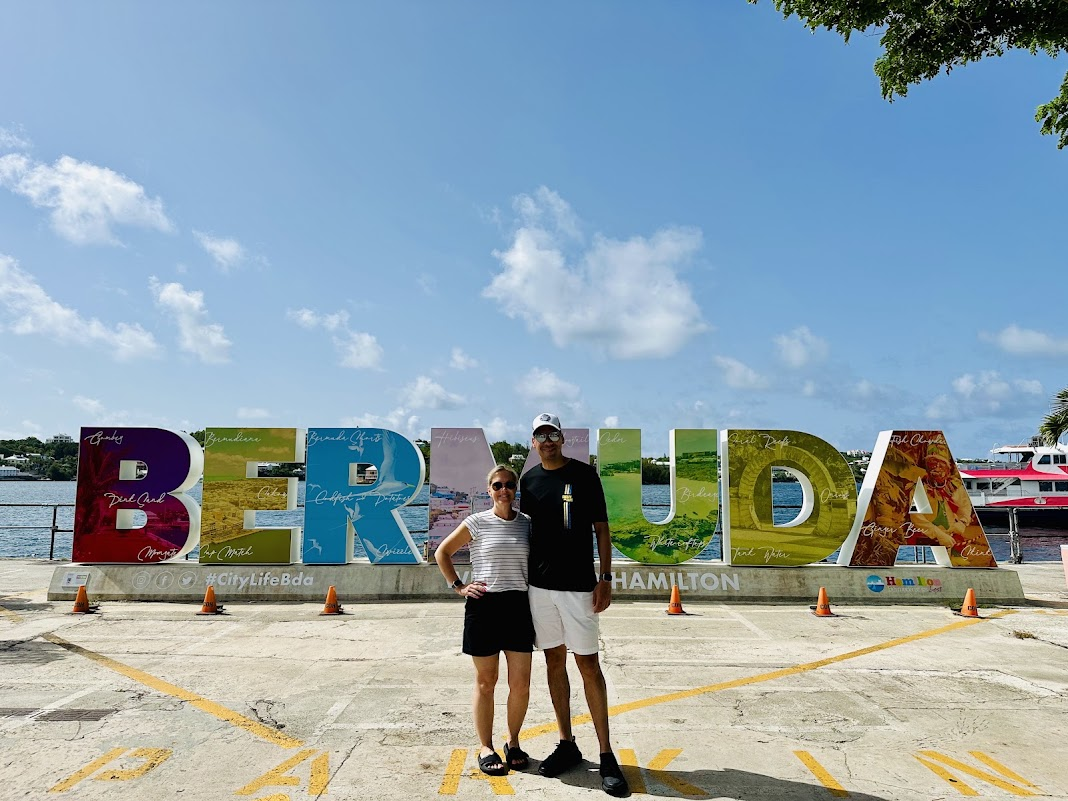 Melissa and her husband in front of the colorful BERMUDA sign in Hamilton