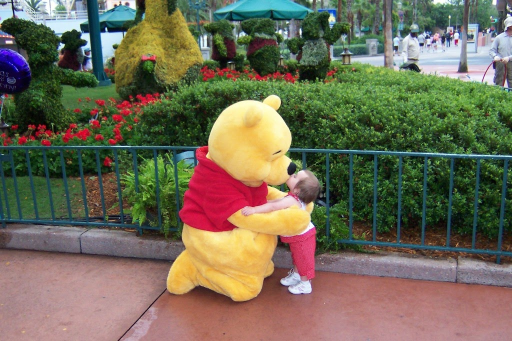 A toddler in red giving Winnie the Pooh a kiss at Walt Disney World